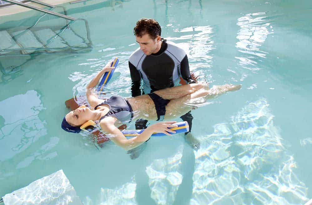 Physiotherapist in swimming pool treats patient with hydrotherapy to aid recovery and rehabilitation for physical and/or neurological injury