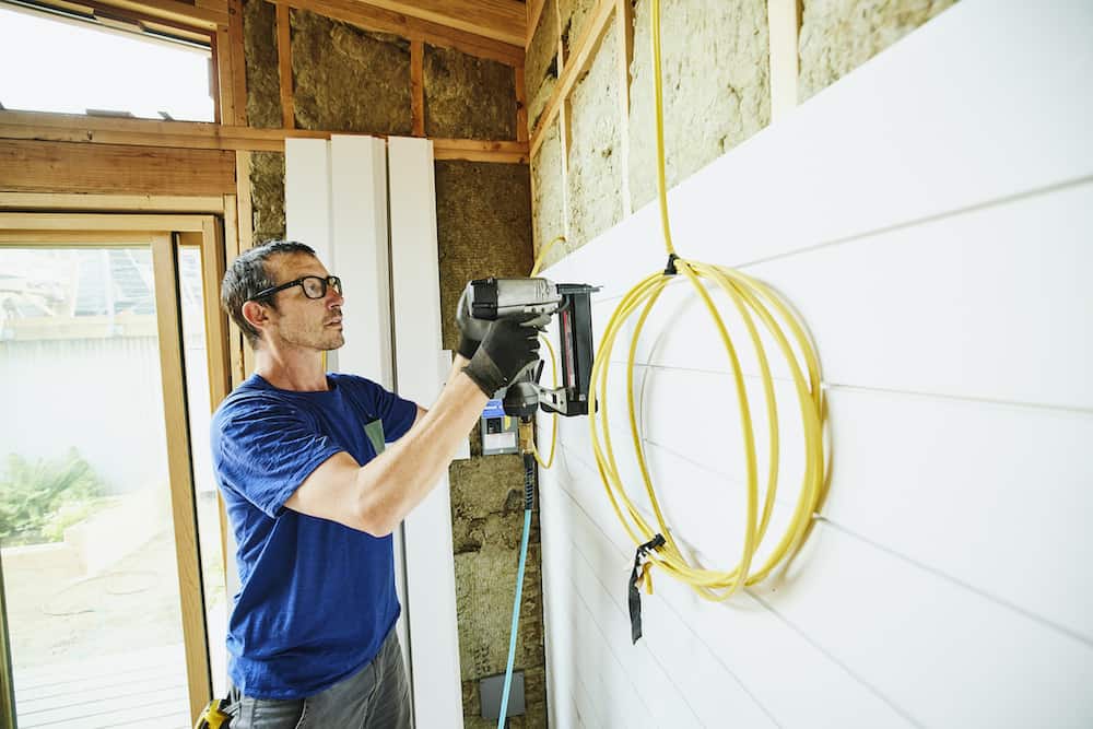 Man using nail gun to install siding during home remodeling project