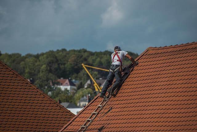 Man on ladder fixing a roof to prevent flashing leaks