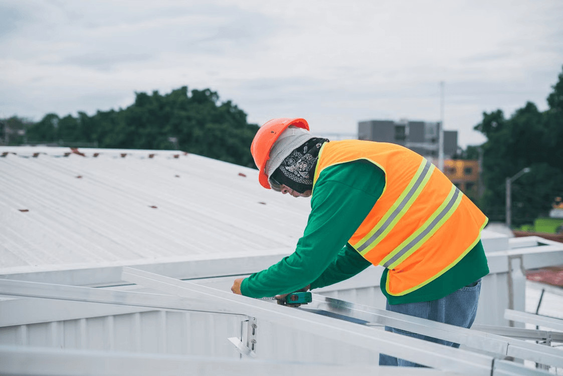 A roofing contractor in a safety vest inspects a