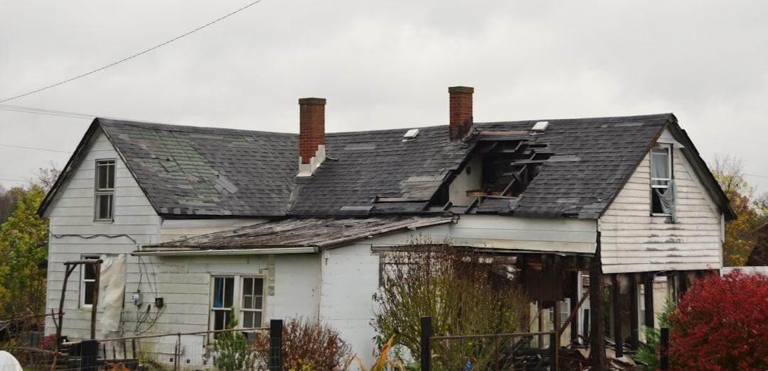 A weathered older house with worn siding and an aging roof in need of repairs
