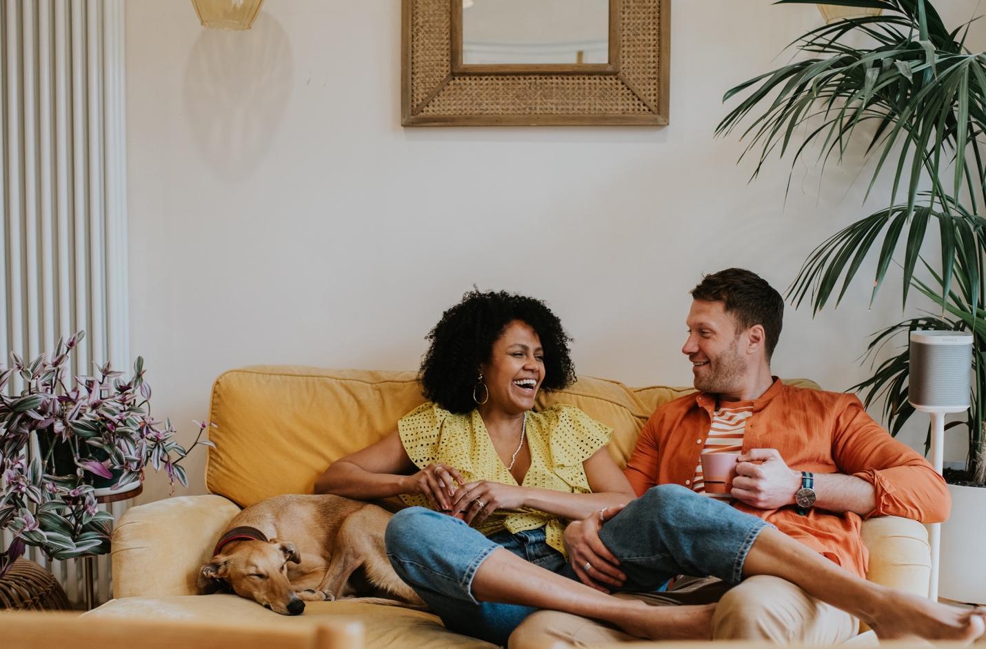 Laughing couple with dog sitting on sofa