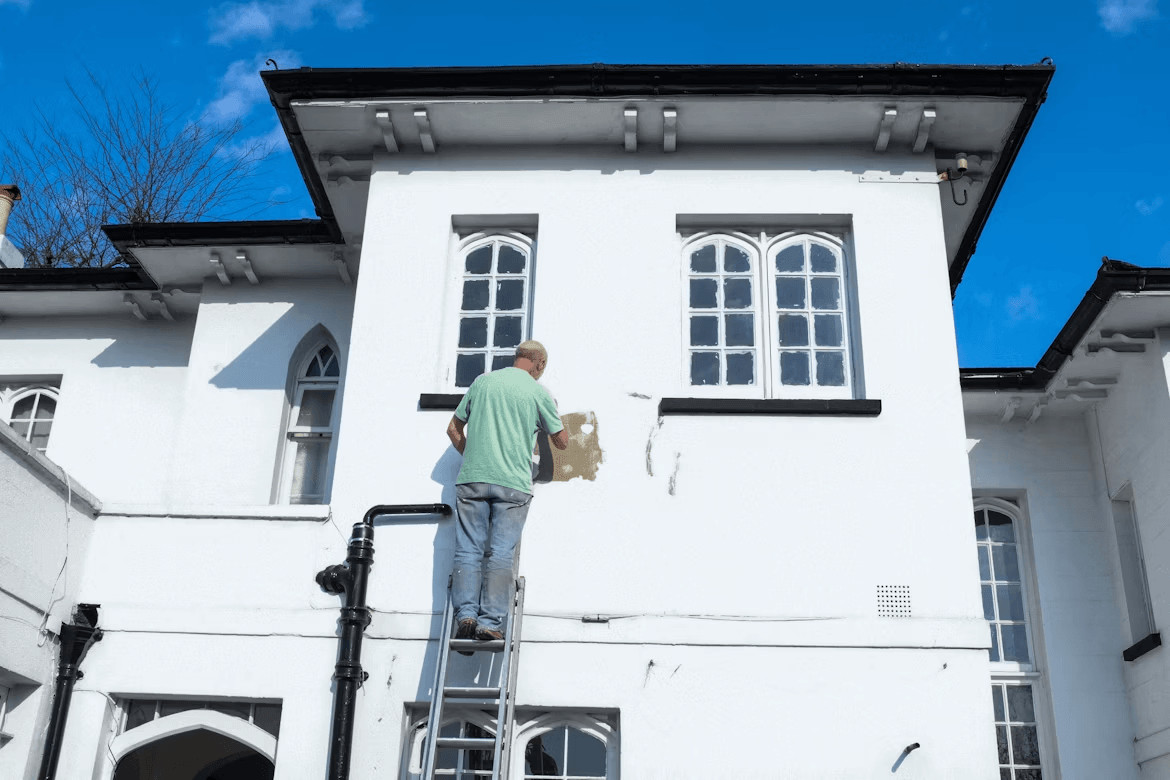 How to Prepare Your Home for a Long-Lasting Paint Job 2 Man on ladder inspecting white home exterior for paint preparation