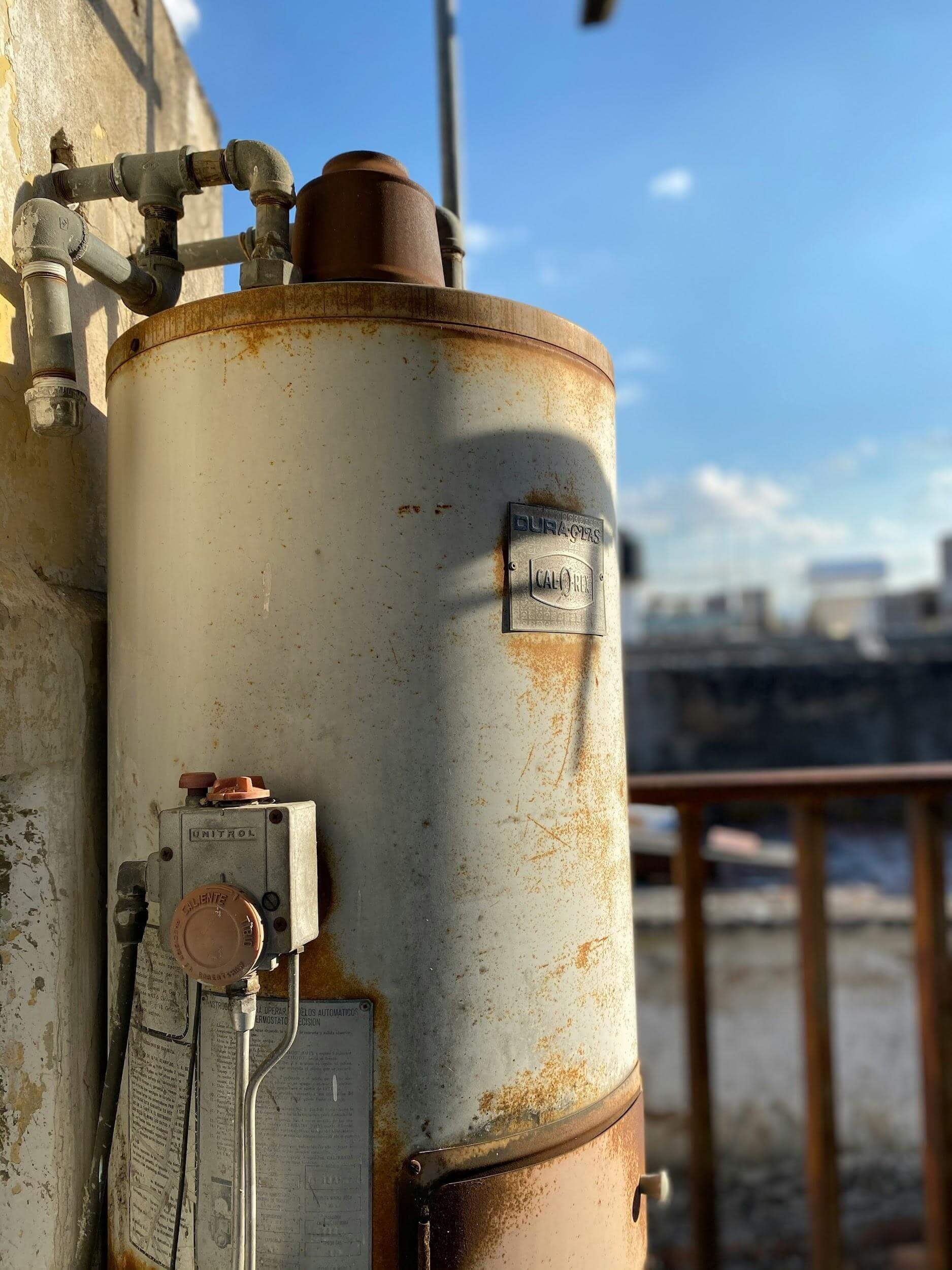 Old, rusty water heater tank next to a