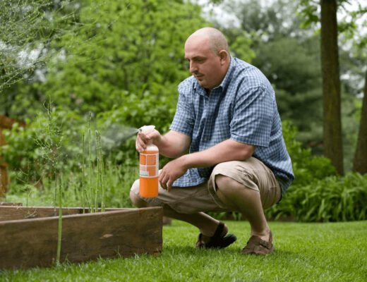 Man kneeling to apply pest control treatment in yard