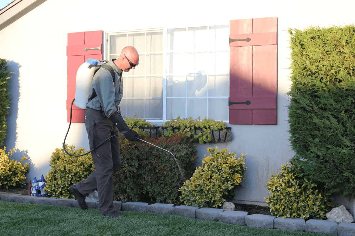 Man spraying for pest control in front of a house