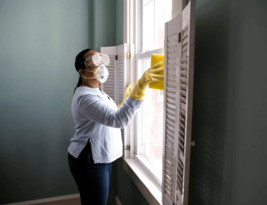 Woman wearing mask and gloves meticulously cleaning a window to