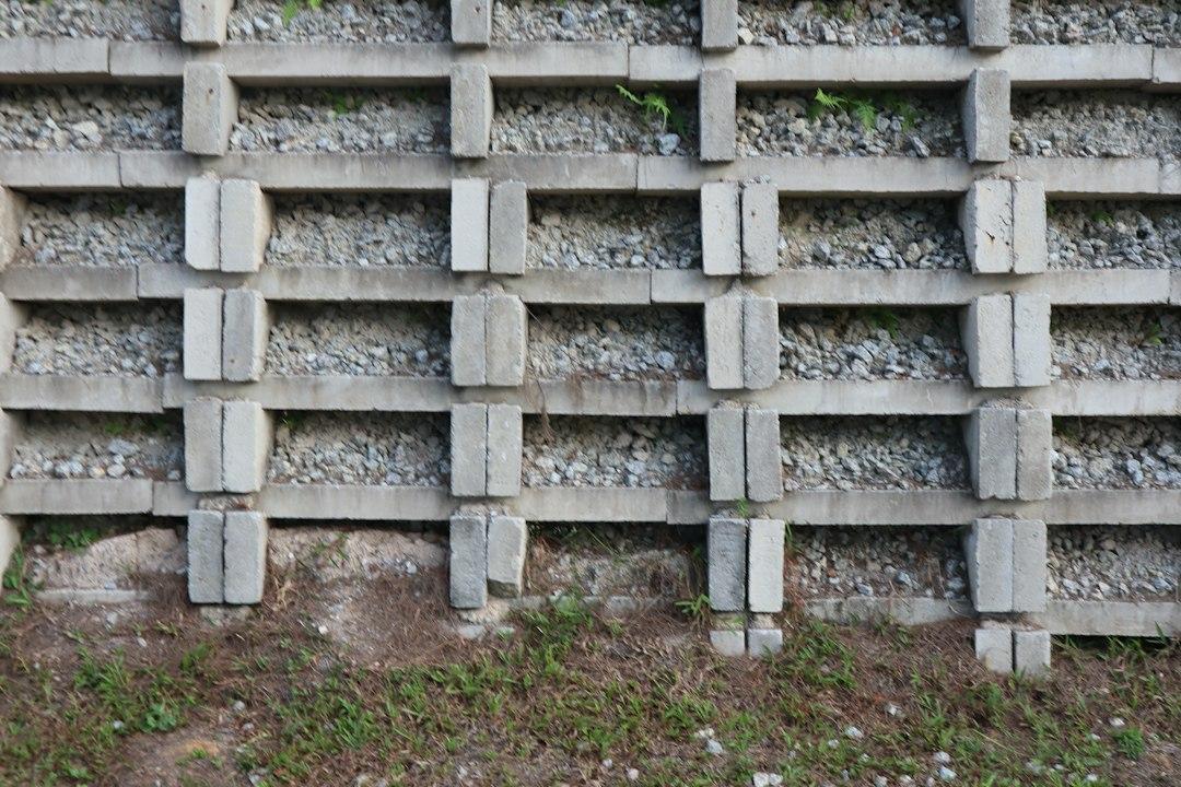 A concrete retaining wall with stacked blocks and gravel fill above grassy ground