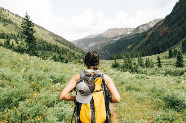 Woman with backpack hiking through a field of wildflowers,